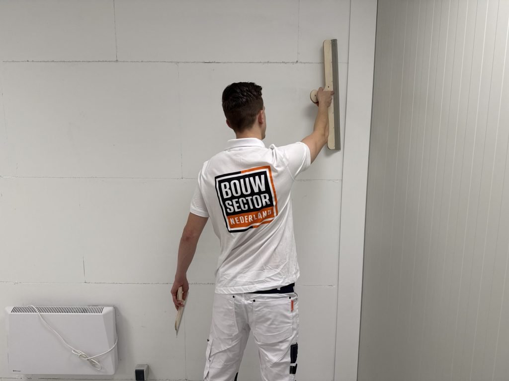 Stukadoor staat met zijn rug naar ons en trekt de pleister op een wand boven een elektrische kachel vlak