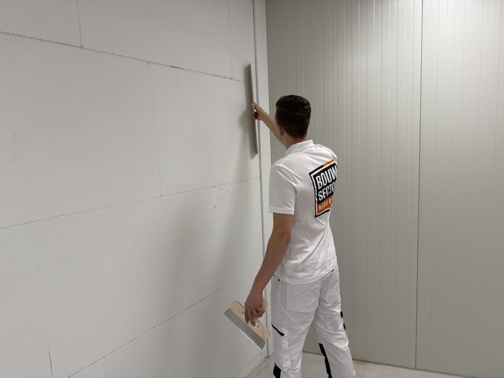 Stukadoor in Bouwsector-polo zet een rei hoog tegen een wand van gipsblokken