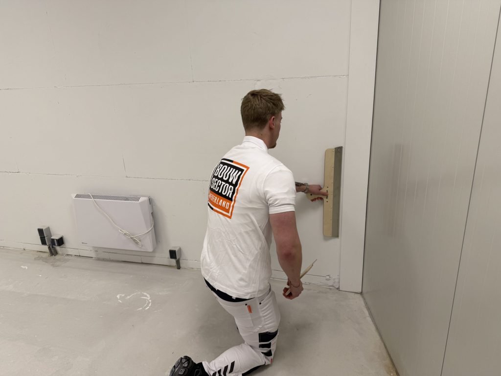 Stukadoor zit op zijn knie en werkt met een rei het onderste deel van een wand af