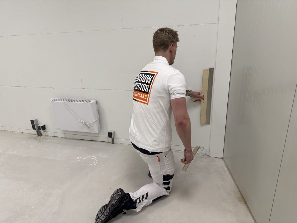 Stukadoor knielt bij de plint en trekt de laatste strook pleister met de rei glad