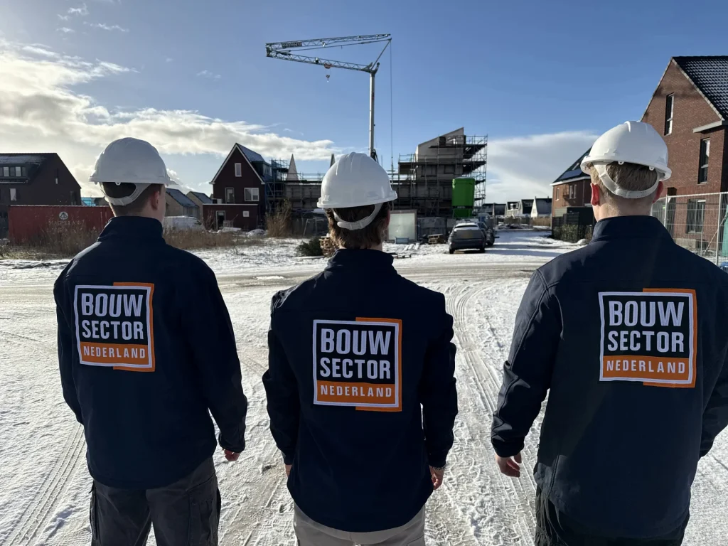 Drie vakmensen van Bouwsector Nederland met witte helm op een nieuwbouwlocatie met hijskraan
