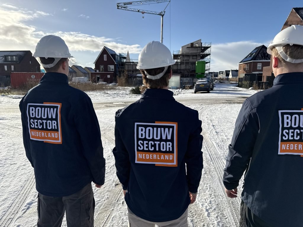 Drie mensen van Bouwsector Nederland in werkjassen kijken naar woningen in aanbouw